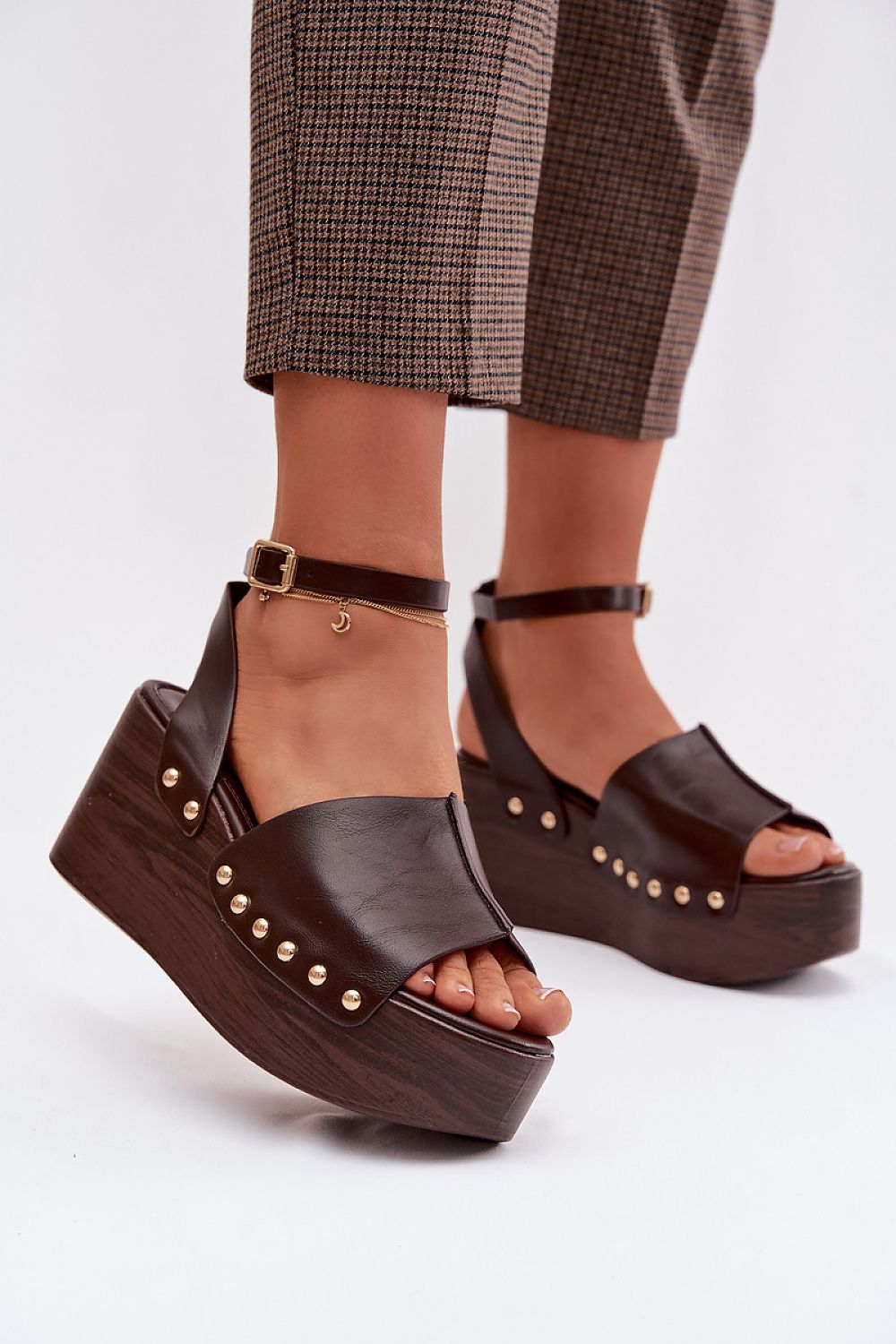 Brown platform sandals with studded details worn with plaid pants on a white background