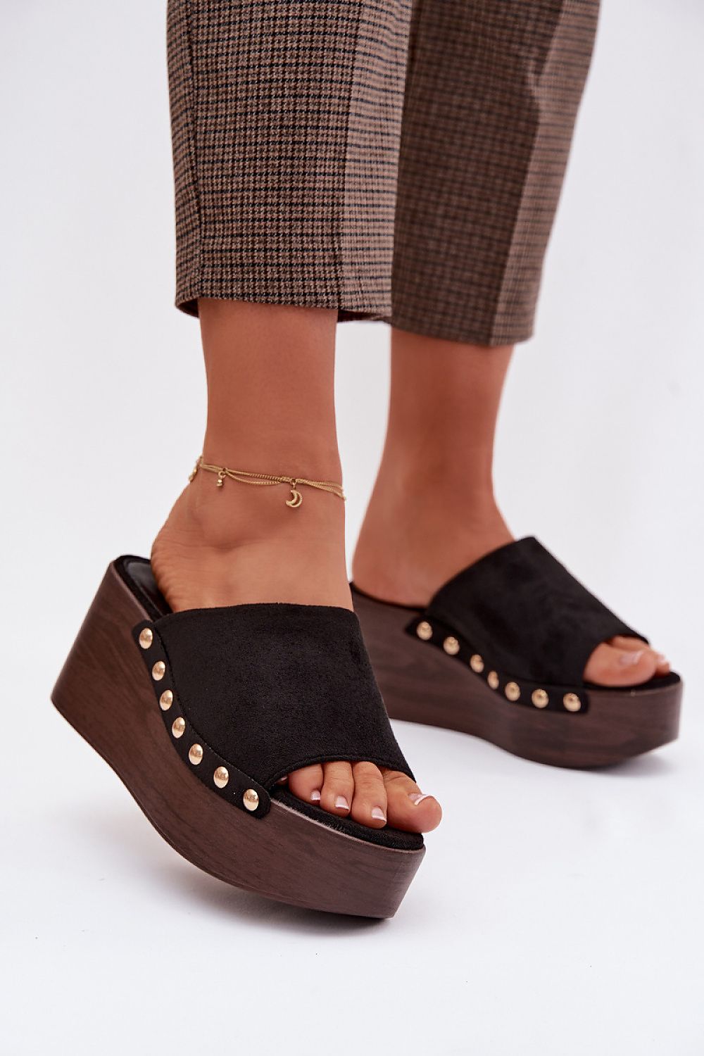 Black wedge sandals with gold studs worn by a person on a white background