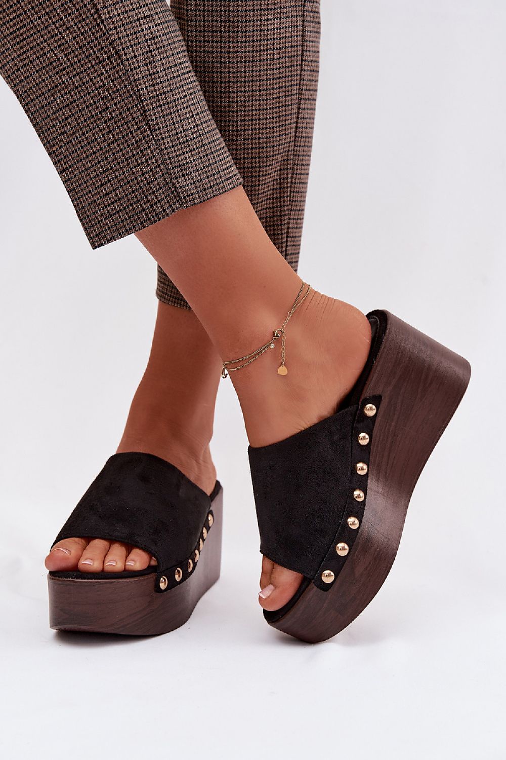 Black platform sandals with wooden soles worn with plaid pants on a white background