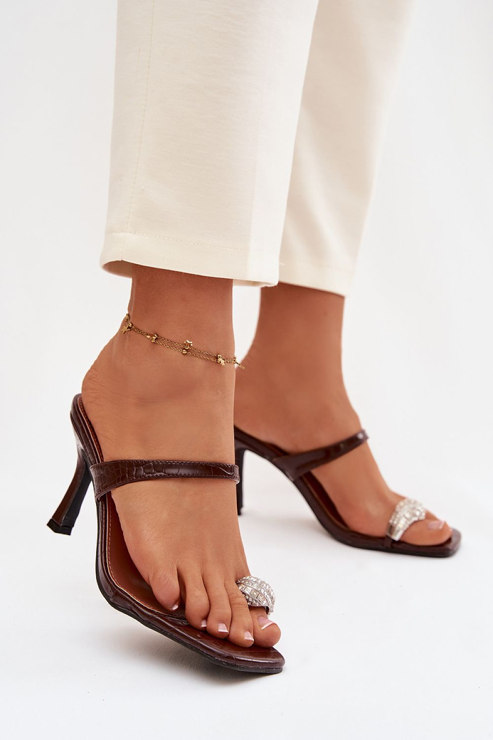 Brown high-heeled sandals worn with white pants on a light background