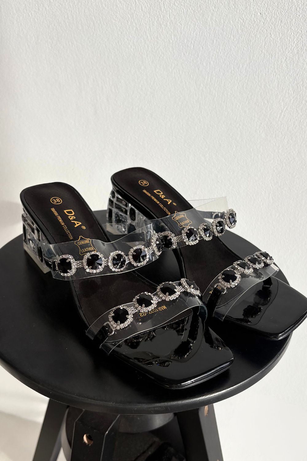 Black sandals with decorative straps on a black stand against a white background