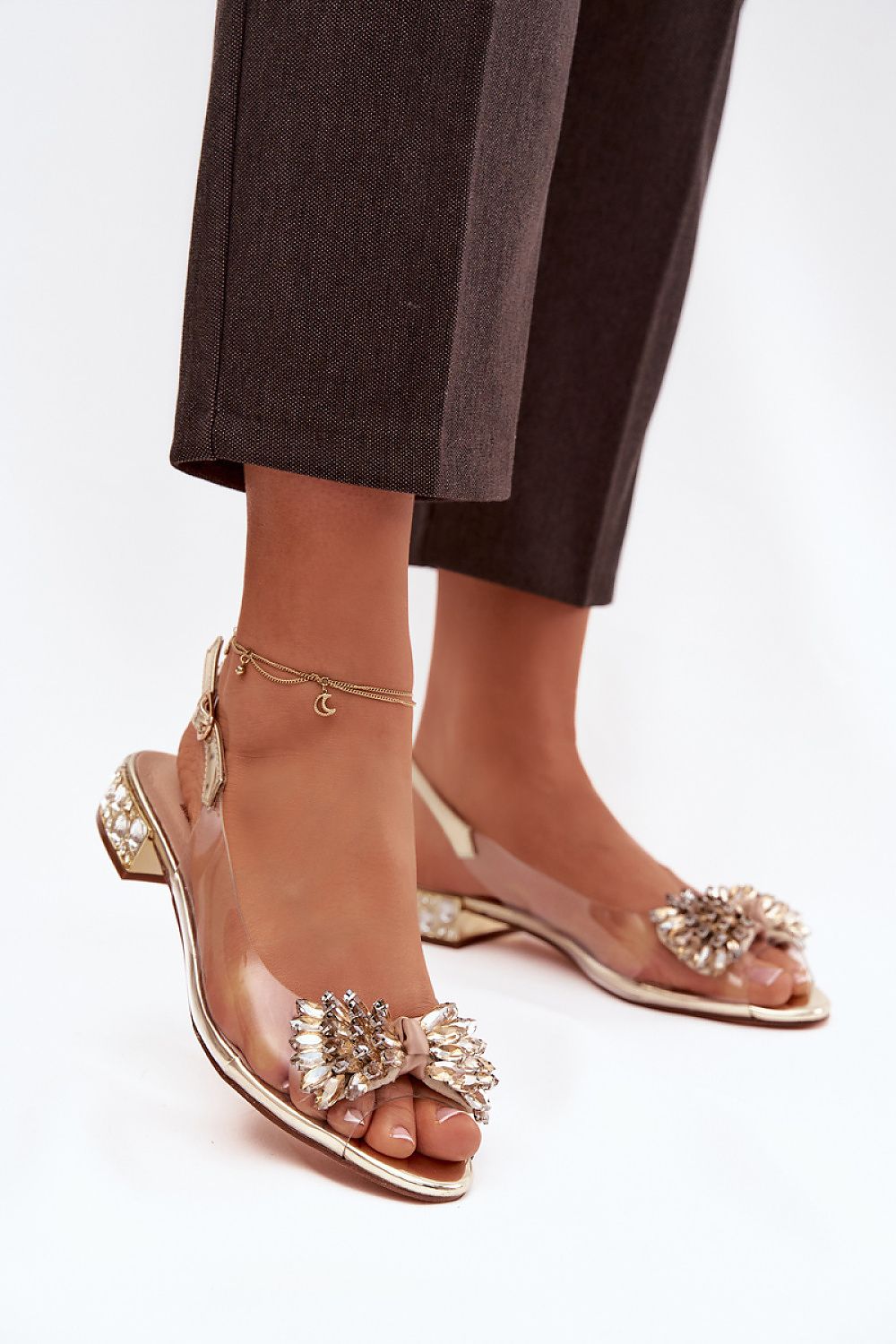 Gold sandals with decorative elements worn by a person on a white background