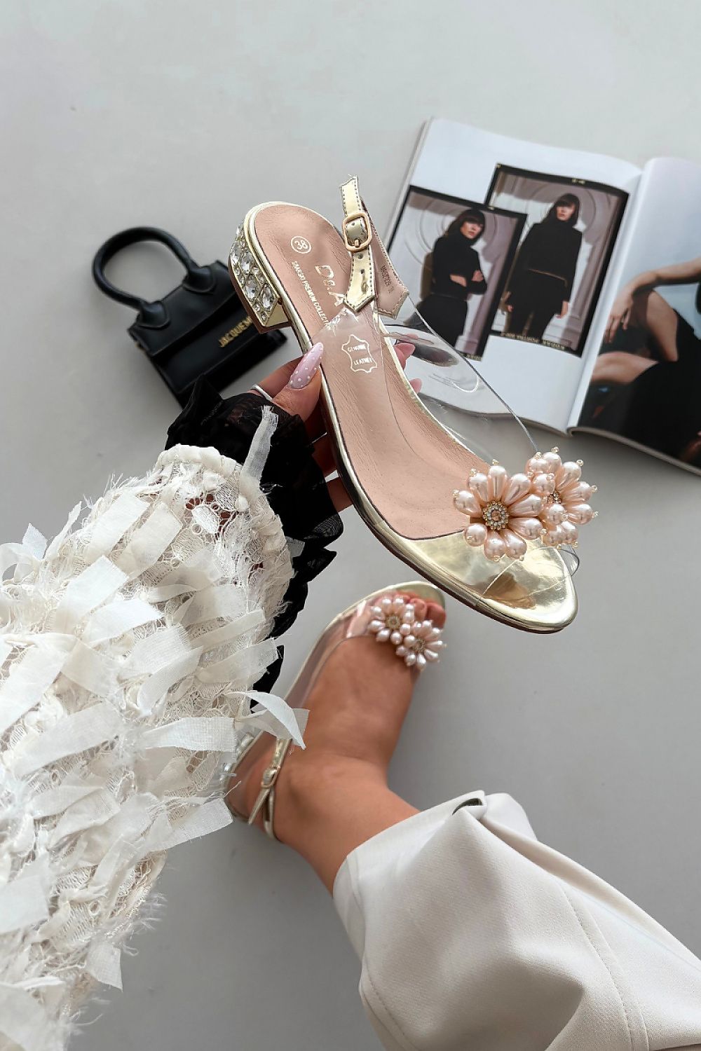 Gold high-heeled shoe with pearl embellishments on a neutral background