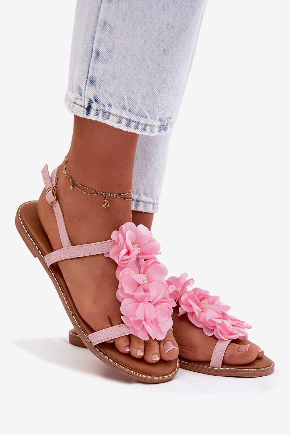 Pink sandals with floral details worn with light blue jeans on a white background