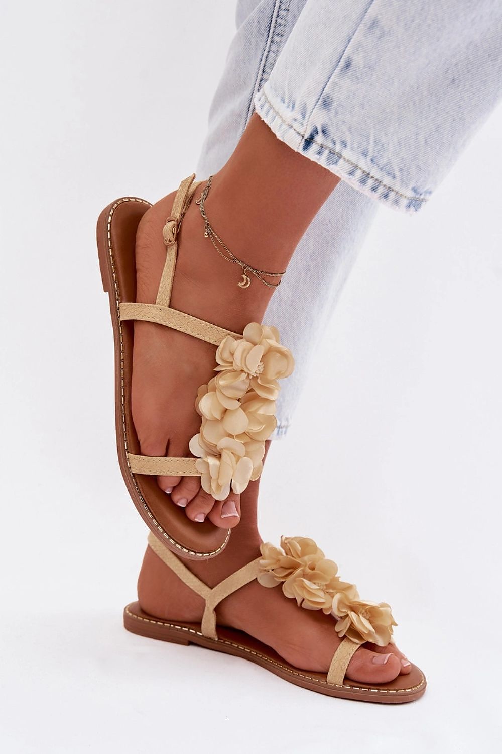 Beige sandals with floral details worn by a person on a white background