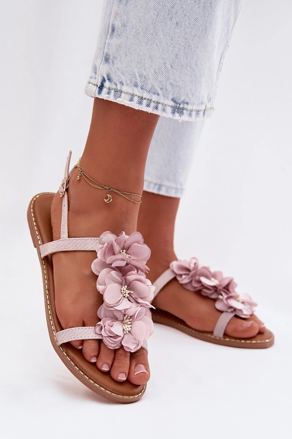 Pink floral sandals worn with light blue jeans on a white background