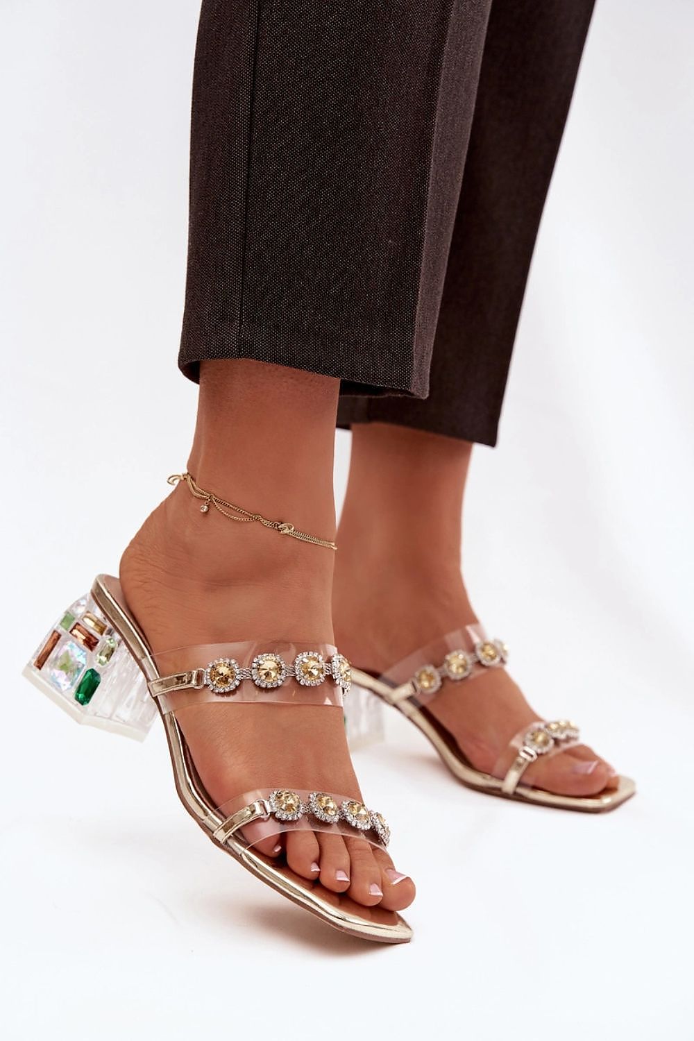 Clear high-heeled sandals with gemstone embellishments on a white background