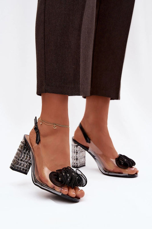 Black high-heeled sandals with clear straps worn by a person on a white background