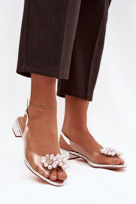 Clear high-heeled sandals with floral embellishments worn by a person in dark pants.