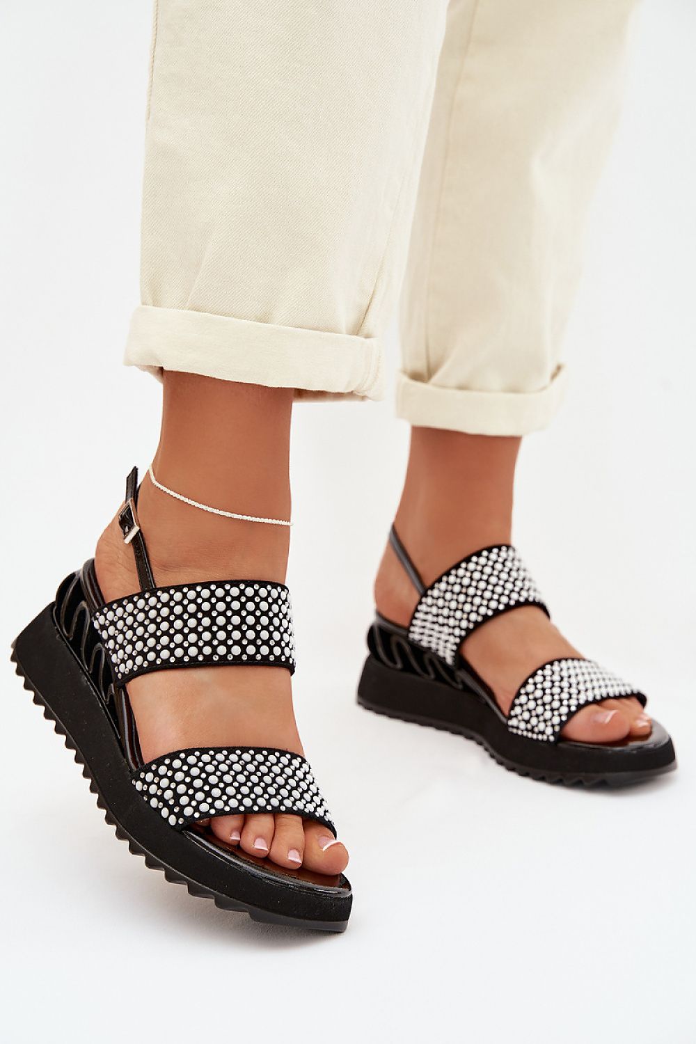 Black sandals with white pattern worn by a person on a white background