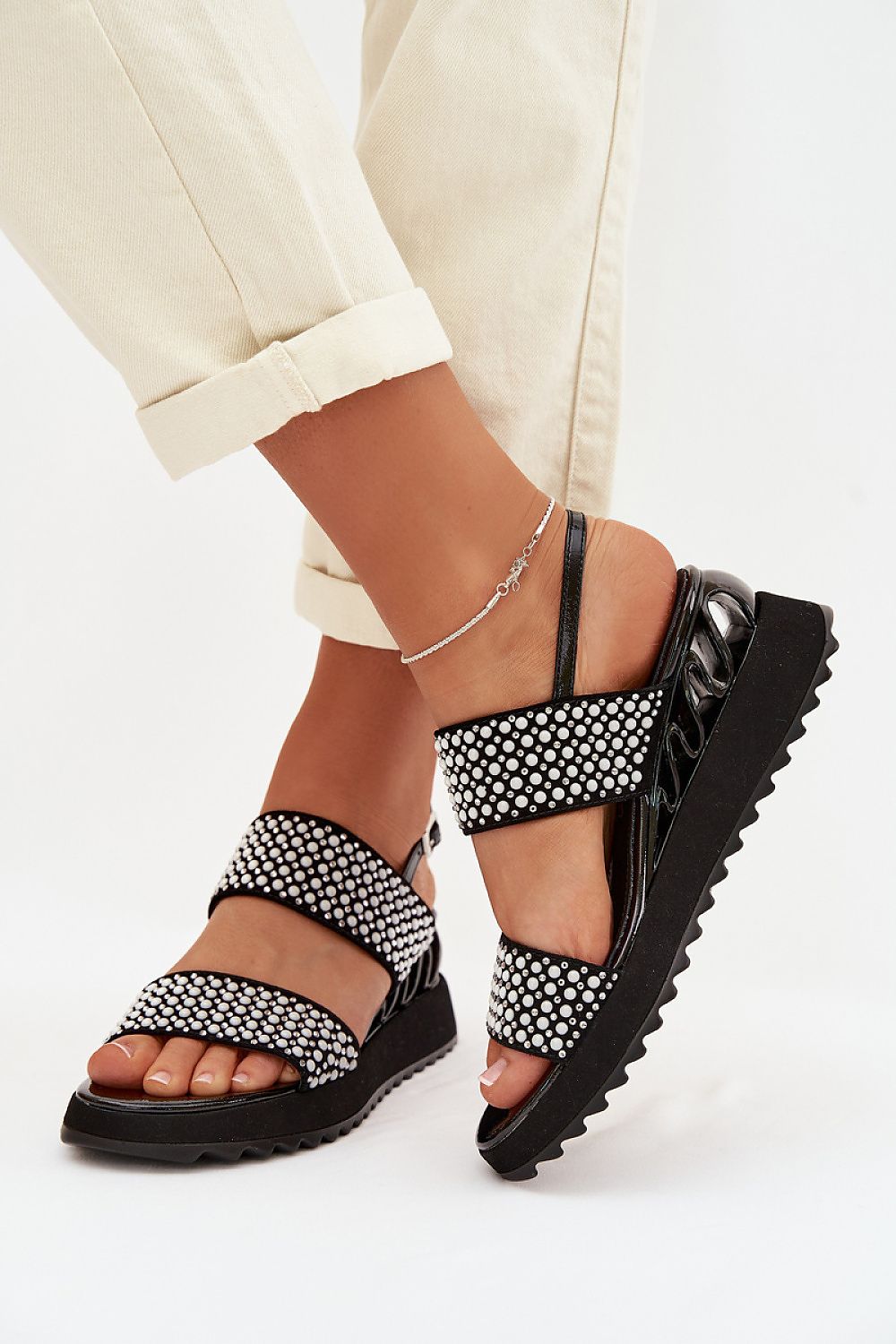 Black sandals with white patterns worn by a person on a white background