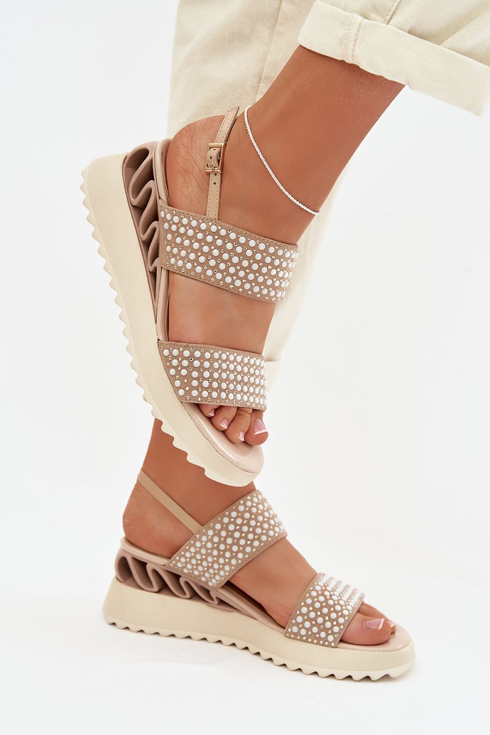 Beige sandals with pearl embellishments worn by a person on a white background
