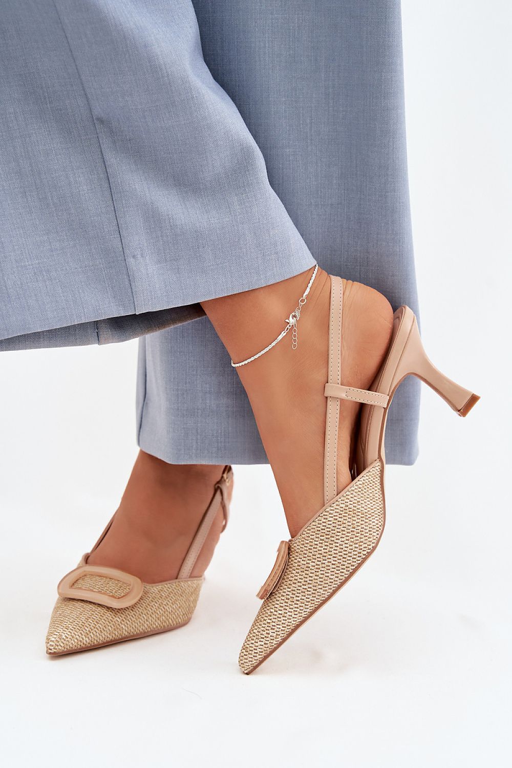 Beige pointed-toe shoes with woven details worn with light blue pants on a white background