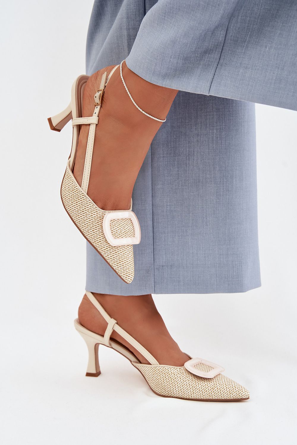 Pair of beige and brown high-heeled shoes worn with a blue outfit on a white background