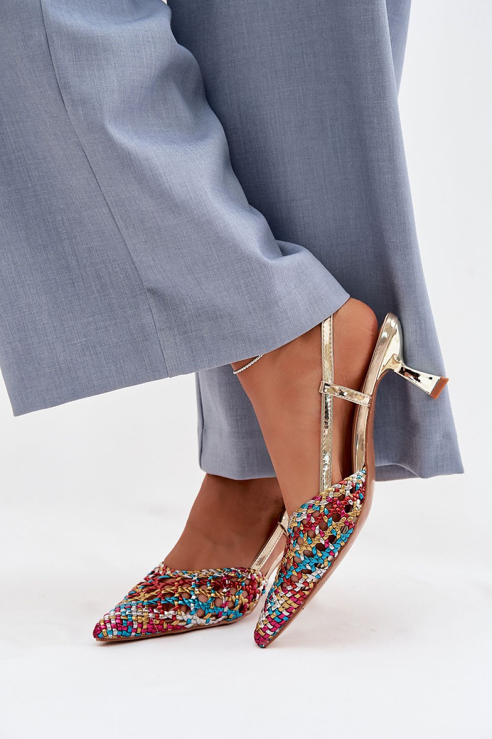 Multicolored embellished shoes worn with gray pants on a white background