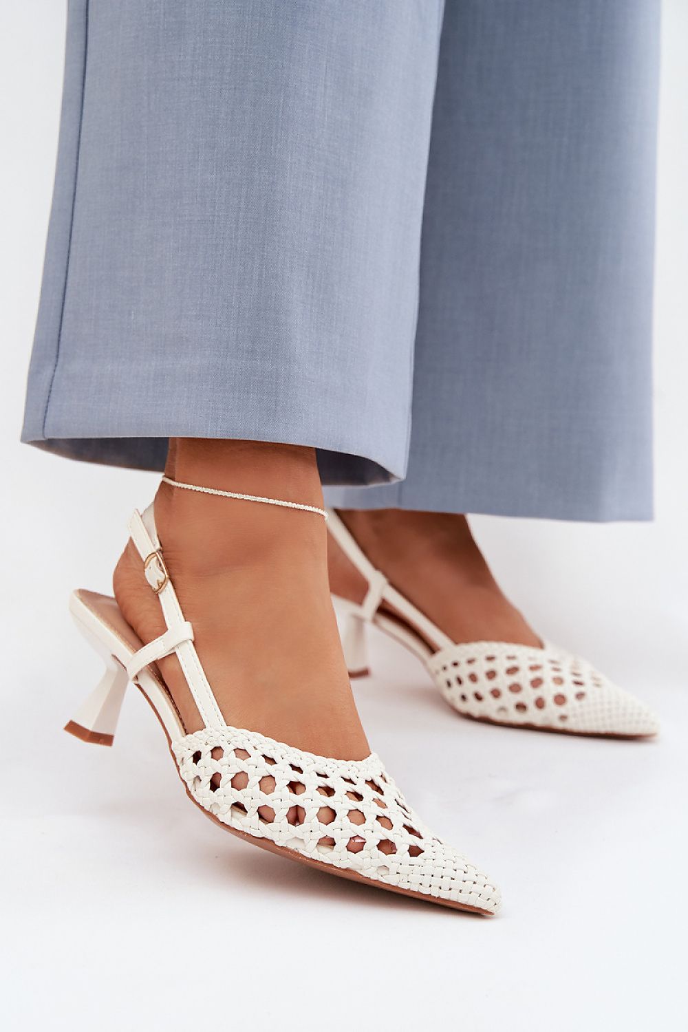 White open-toe high-heeled shoes worn with light blue pants on a white background