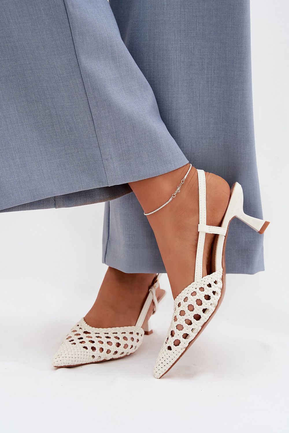 White high-heeled shoes with cut-out design worn with a gray skirt on a white background