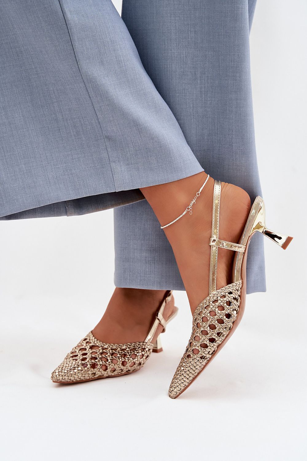 Gold high-heeled shoes with intricate designs worn with blue pants on a white background