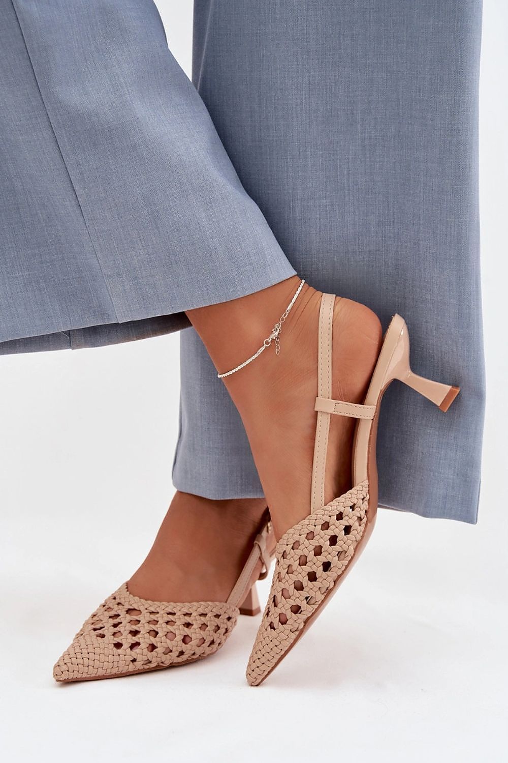 Beige high-heeled shoes with cut-out design worn with blue pants on a white background