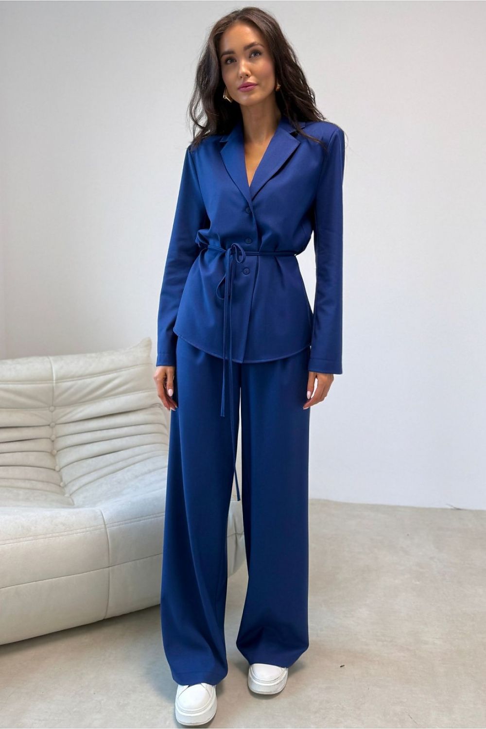 Woman wearing a blue suit standing in a room with a white couch.