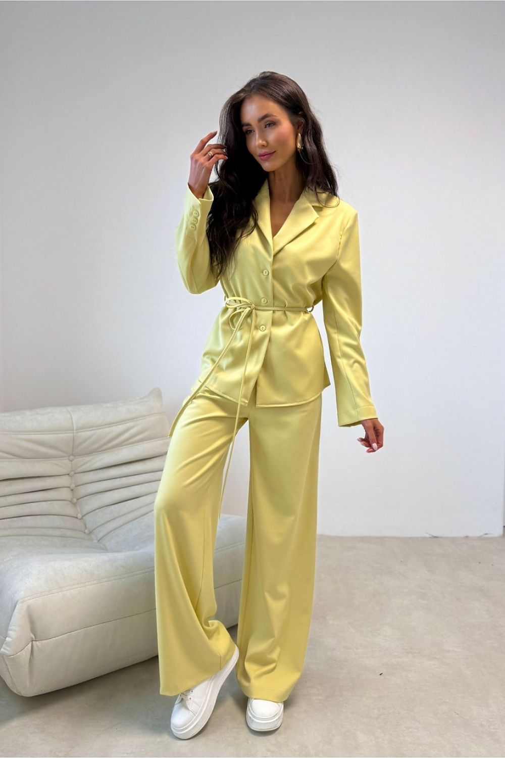 Woman wearing a yellow suit standing in a minimalistic room with a white couch.