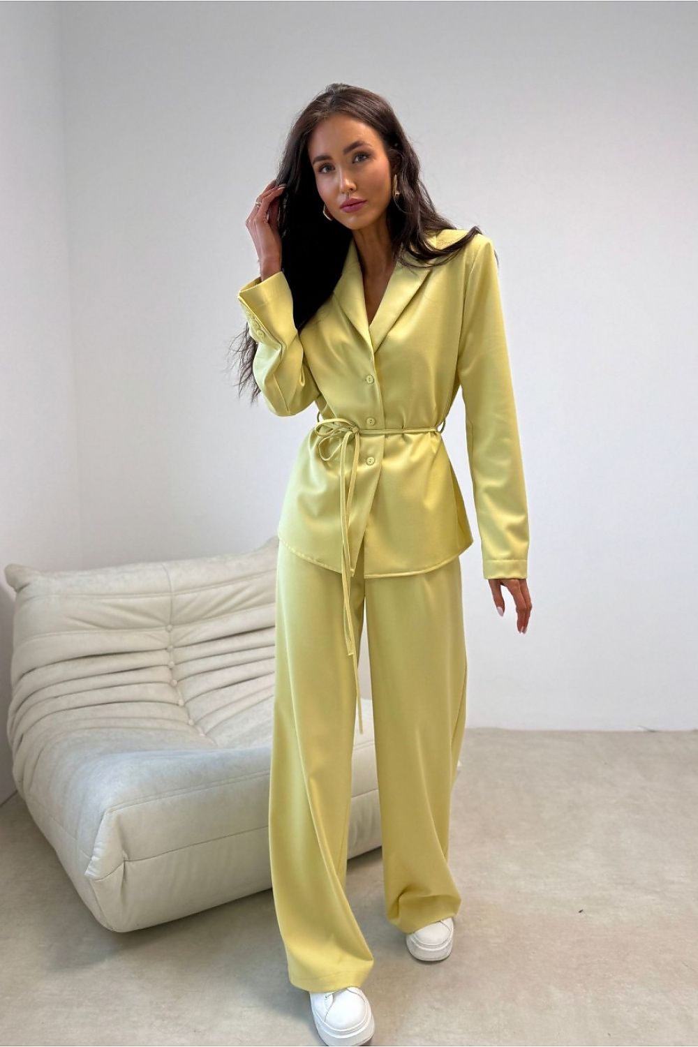 Woman wearing a yellow outfit standing in a minimalistic room with a white sofa.