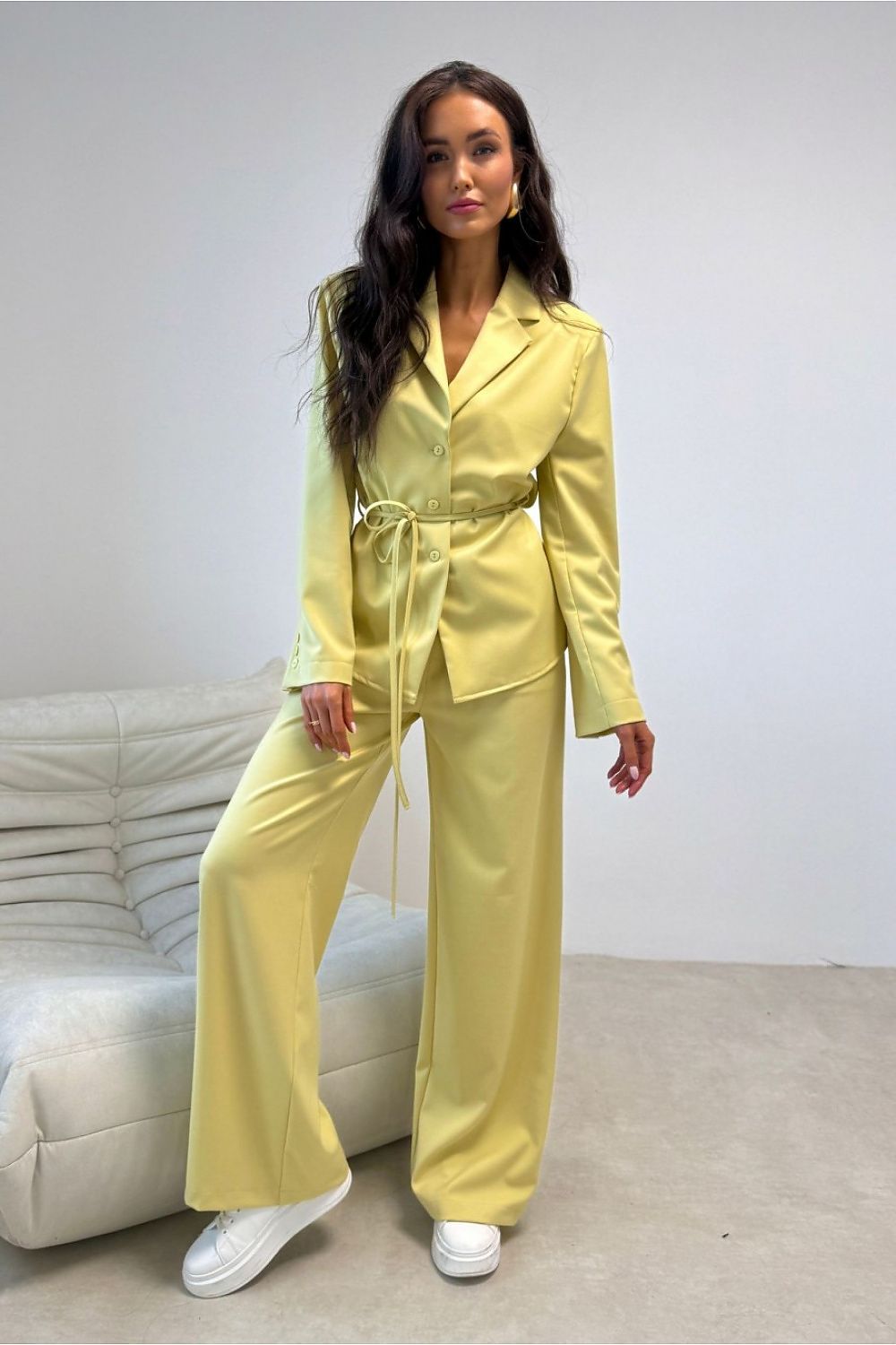 Woman wearing a yellow suit standing in a room with a white couch.