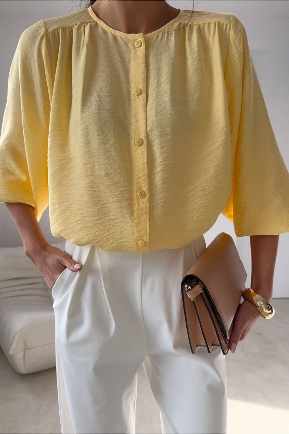 Person wearing a yellow blouse and white pants, holding a brown clutch.
