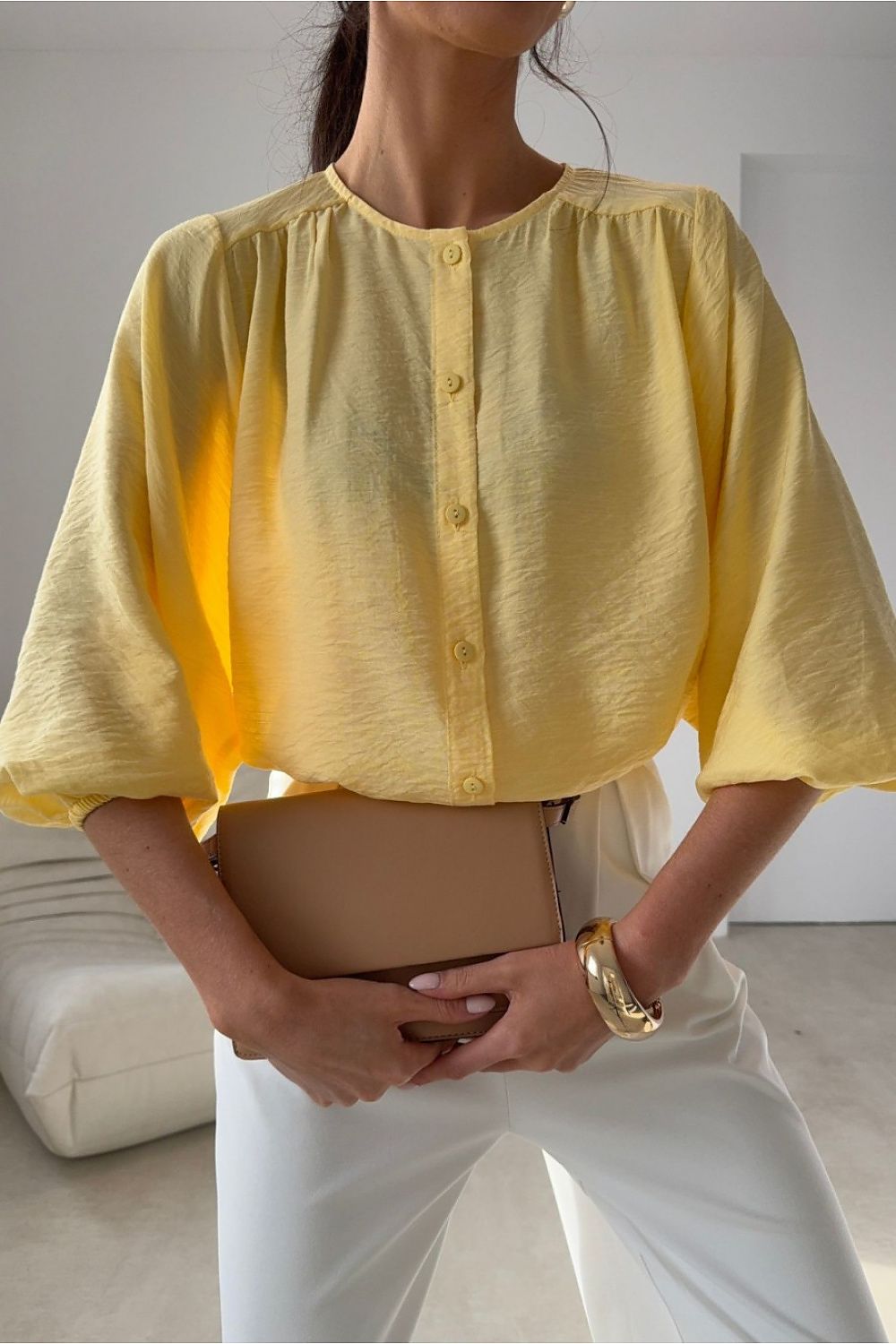 Person wearing a yellow blouse and white pants holding a beige clutch.