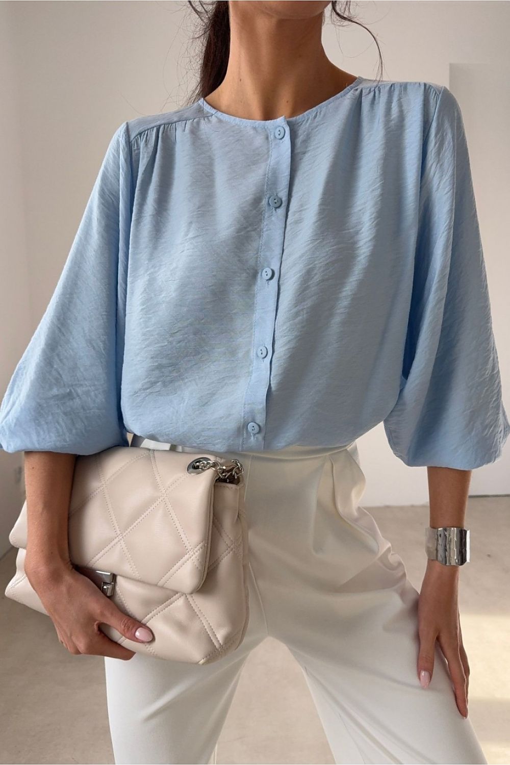 Person wearing a light blue button-up shirt and white pants, holding a beige clutch.