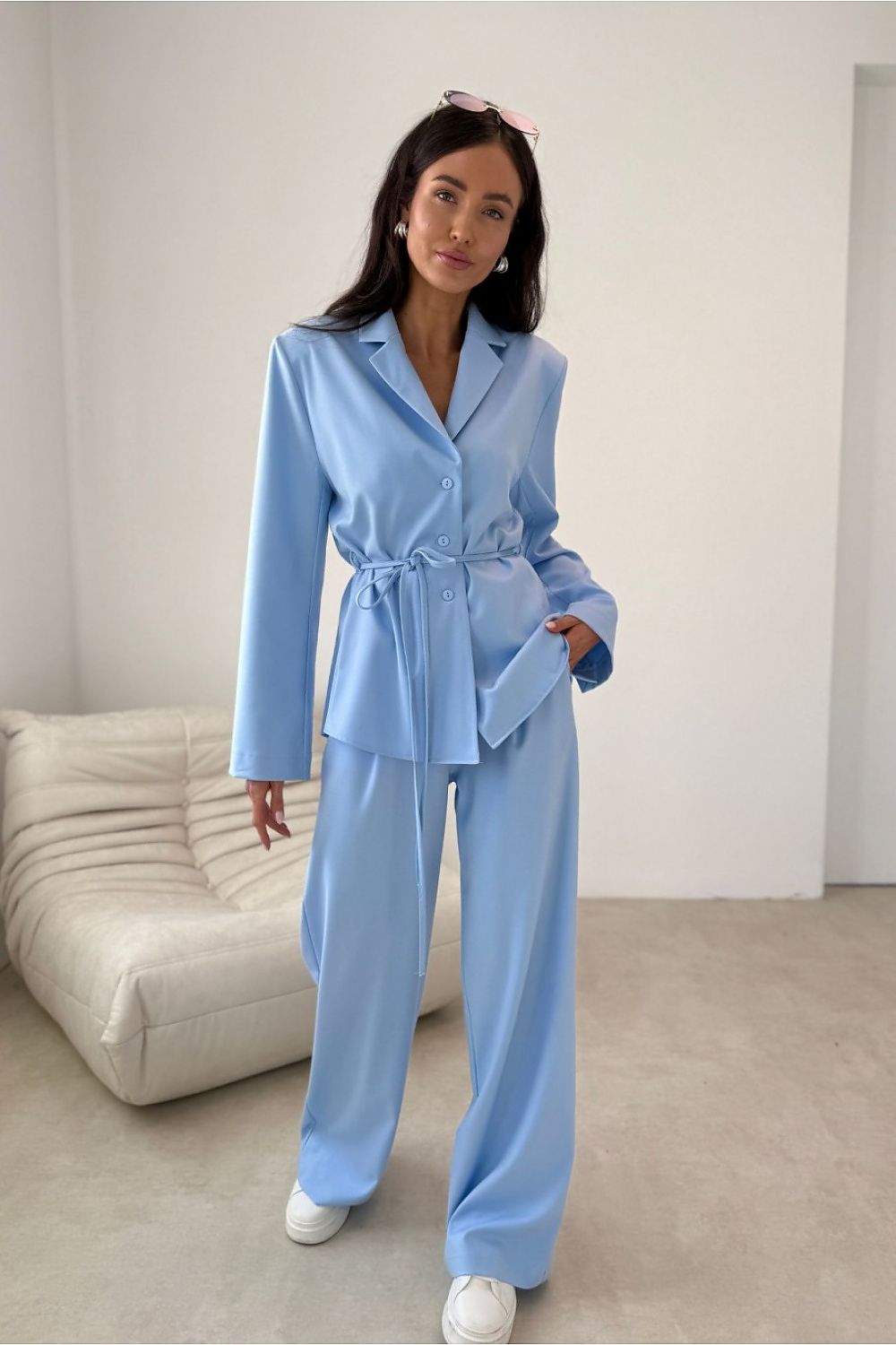 Woman wearing a light blue suit standing in a minimalistic room with a white sofa.