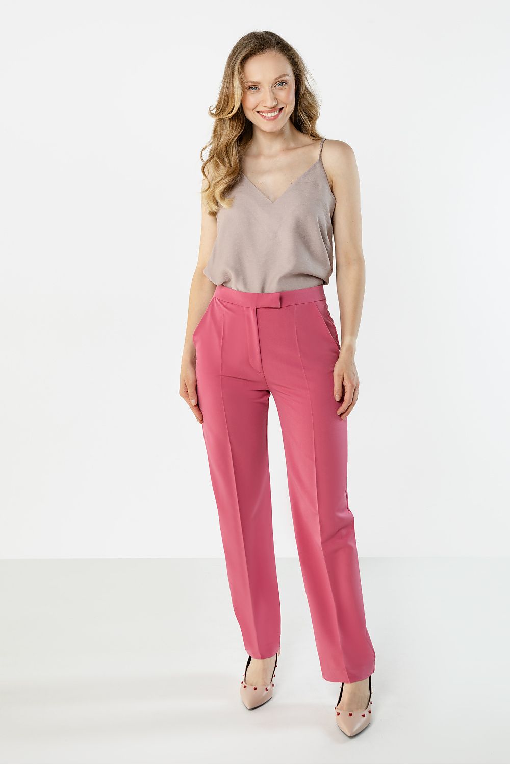 Woman wearing a beige top and pink pants on a white background