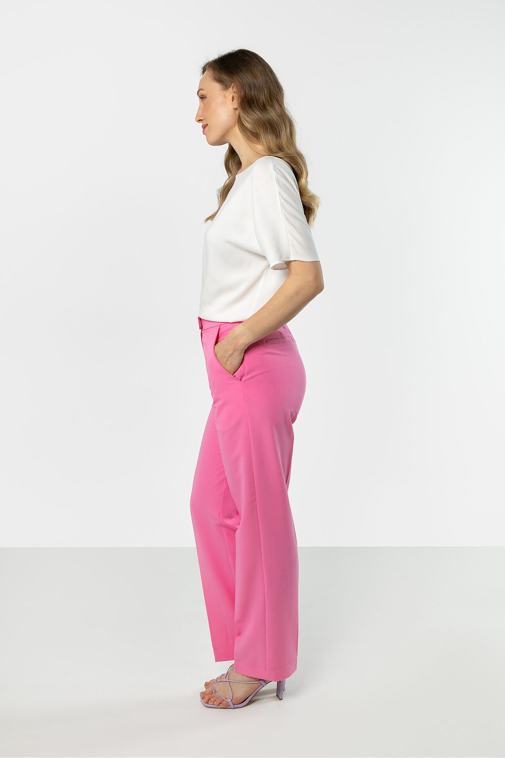 Woman wearing a white top and pink pants on a white background