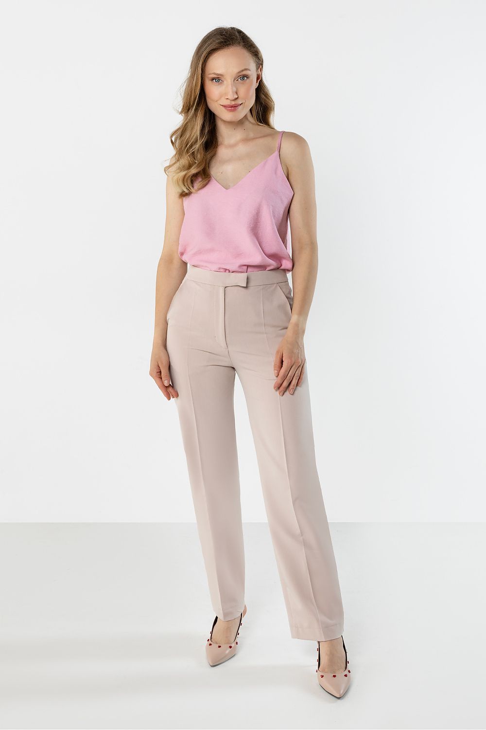 Woman wearing a pink top and beige pants on a white background