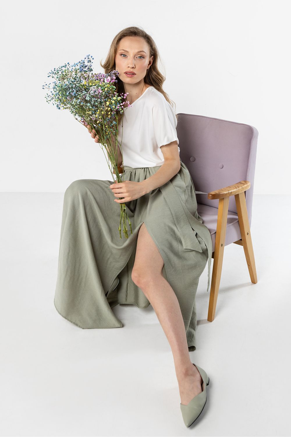 Woman holding flowers and wearing a white top and green skirt on a white background