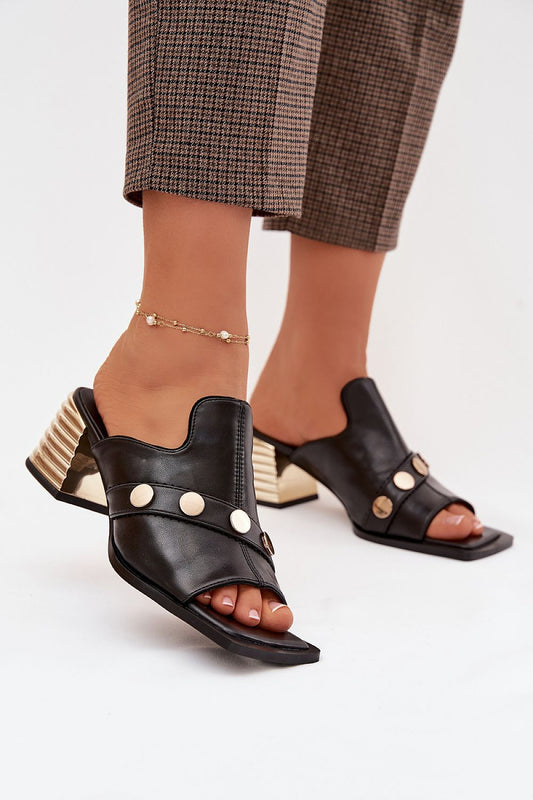 Black open-toe high-heeled shoes with gold accents worn by a person on a white background