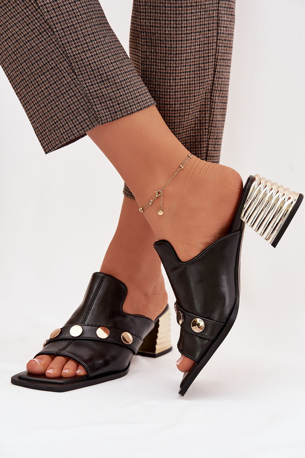 Black open-toe high-heeled shoes with gold accents worn by a person on a white background