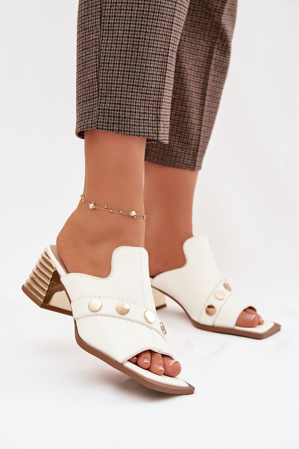 White open-toe shoes with brown soles worn by a person in plaid pants on a light background