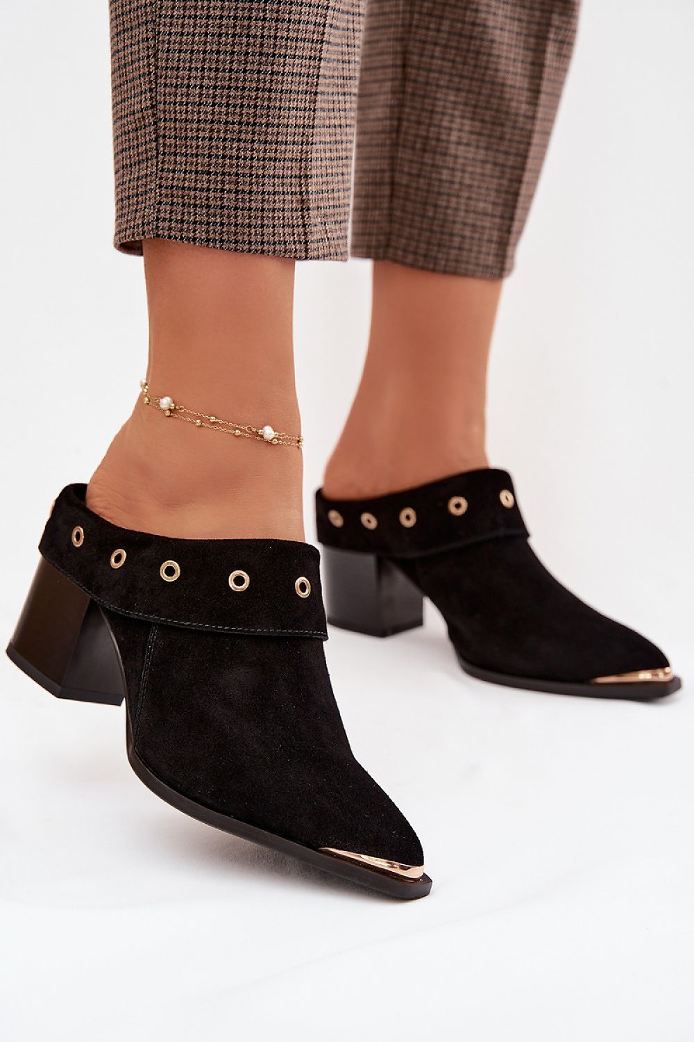 Black suede ankle boots with gold accents worn by a person on a white background