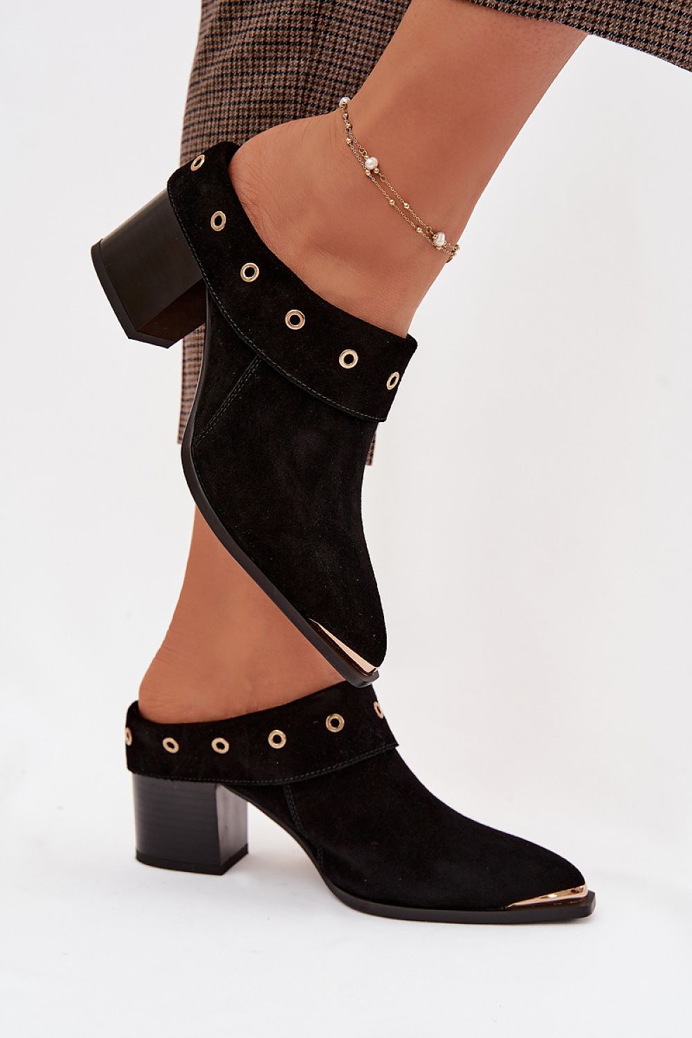 Black suede ankle boots with decorative grommets worn by a person on a white background