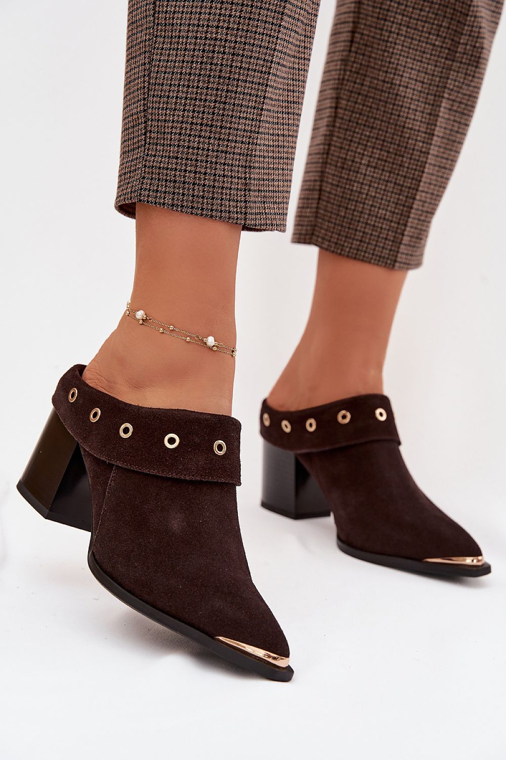 Brown suede ankle boots with gold accents worn with plaid pants on a white background