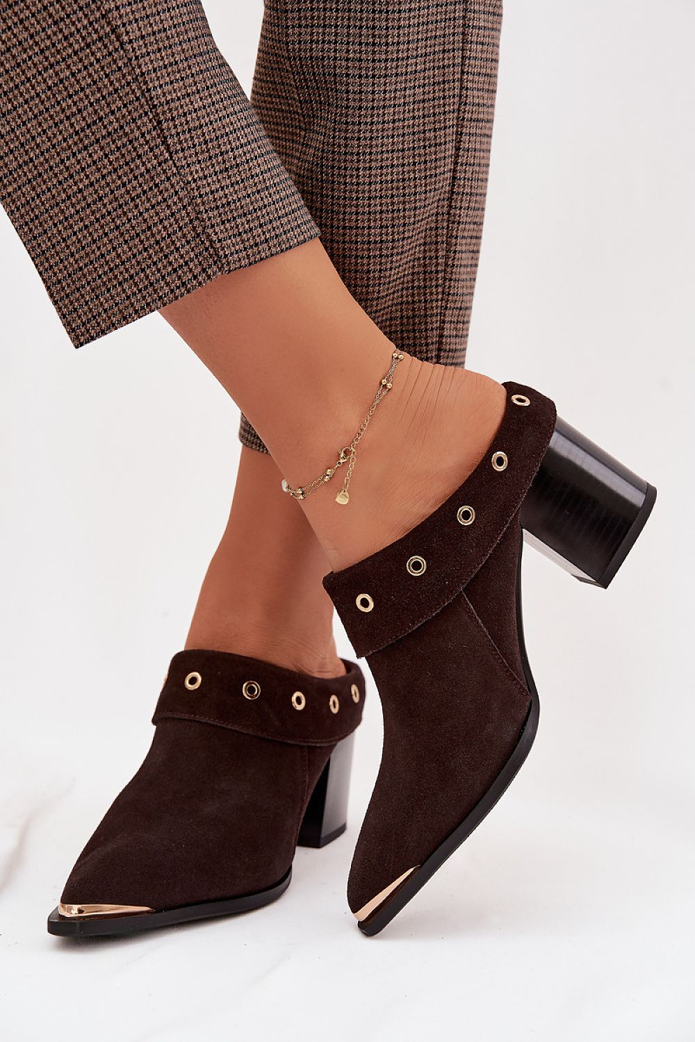 Brown suede boots with decorative straps worn by a person on a white background