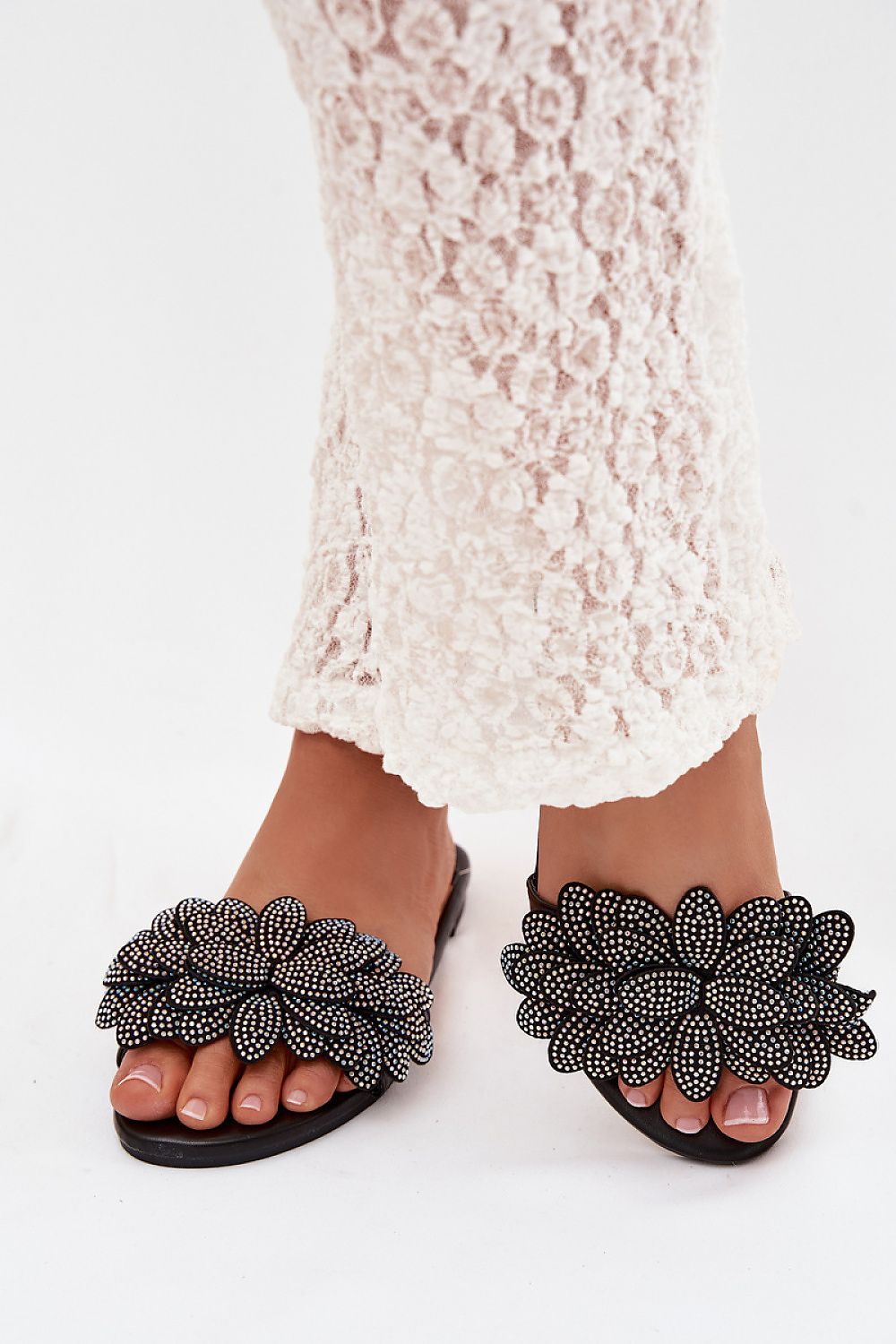 Black beaded sandals worn with a white lace dress on a white background
