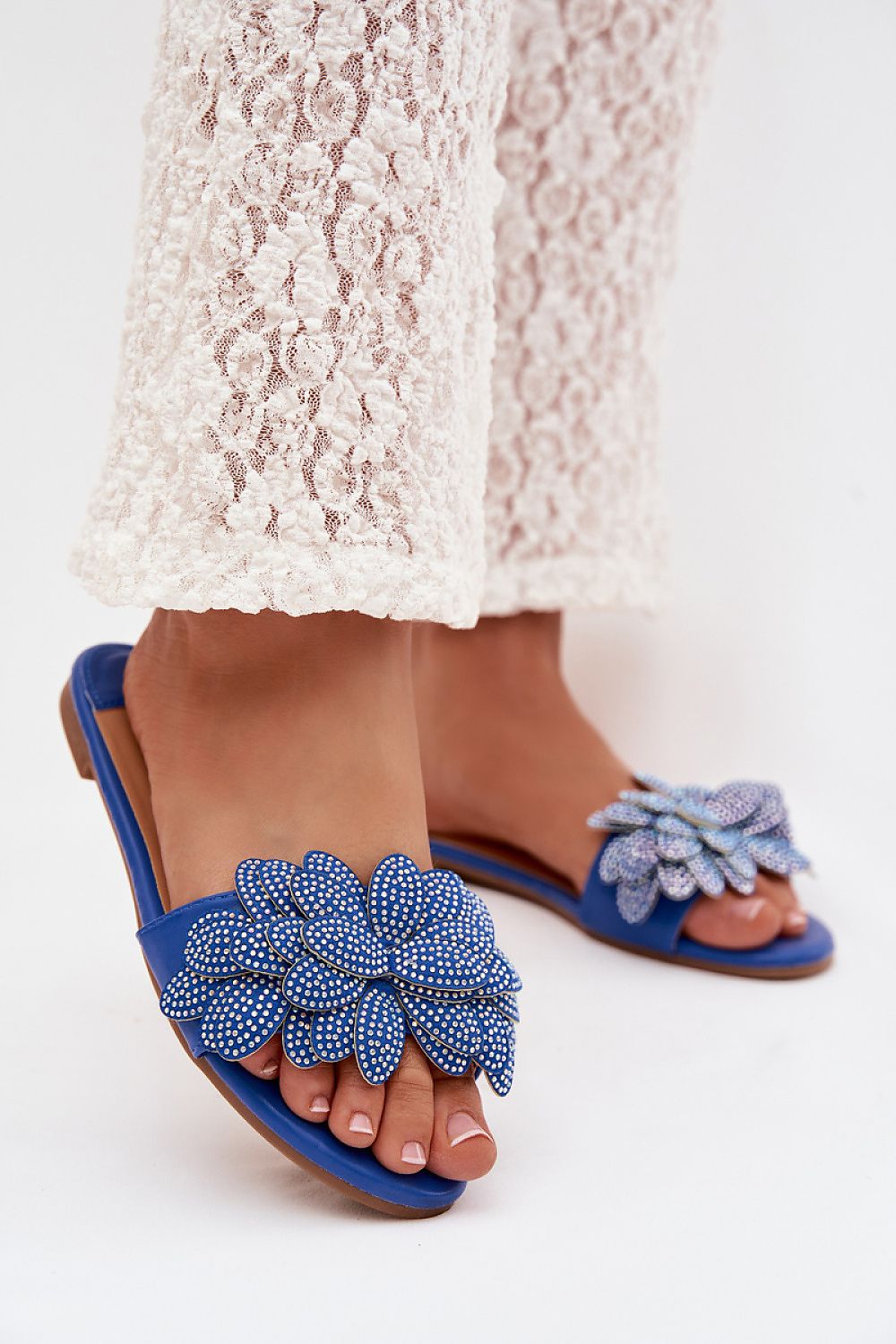 Blue sandals with floral embellishments worn with a white lace skirt on a white background
