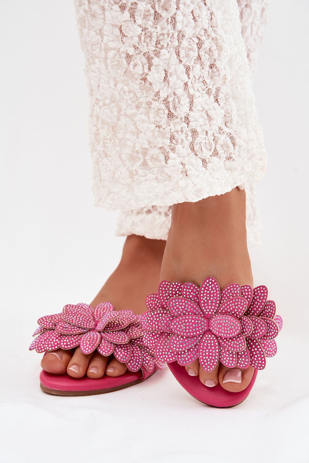 Pink floral sandals with beaded details worn with a white lace dress on a white background