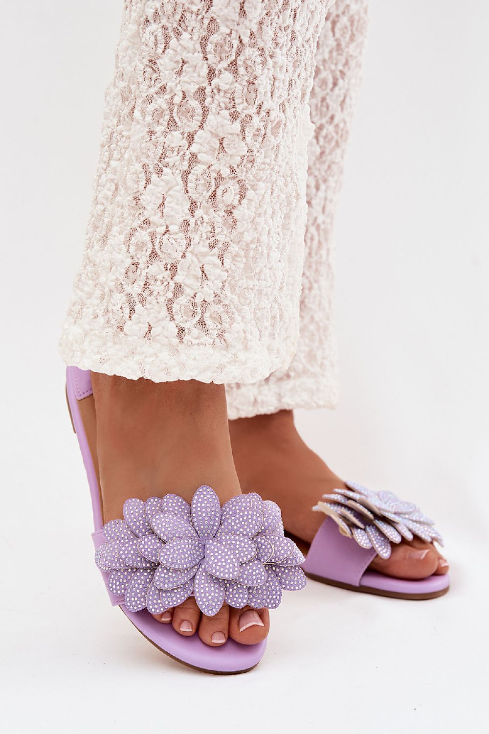 Purple sandals with floral embellishments worn with a lace skirt on a white background
