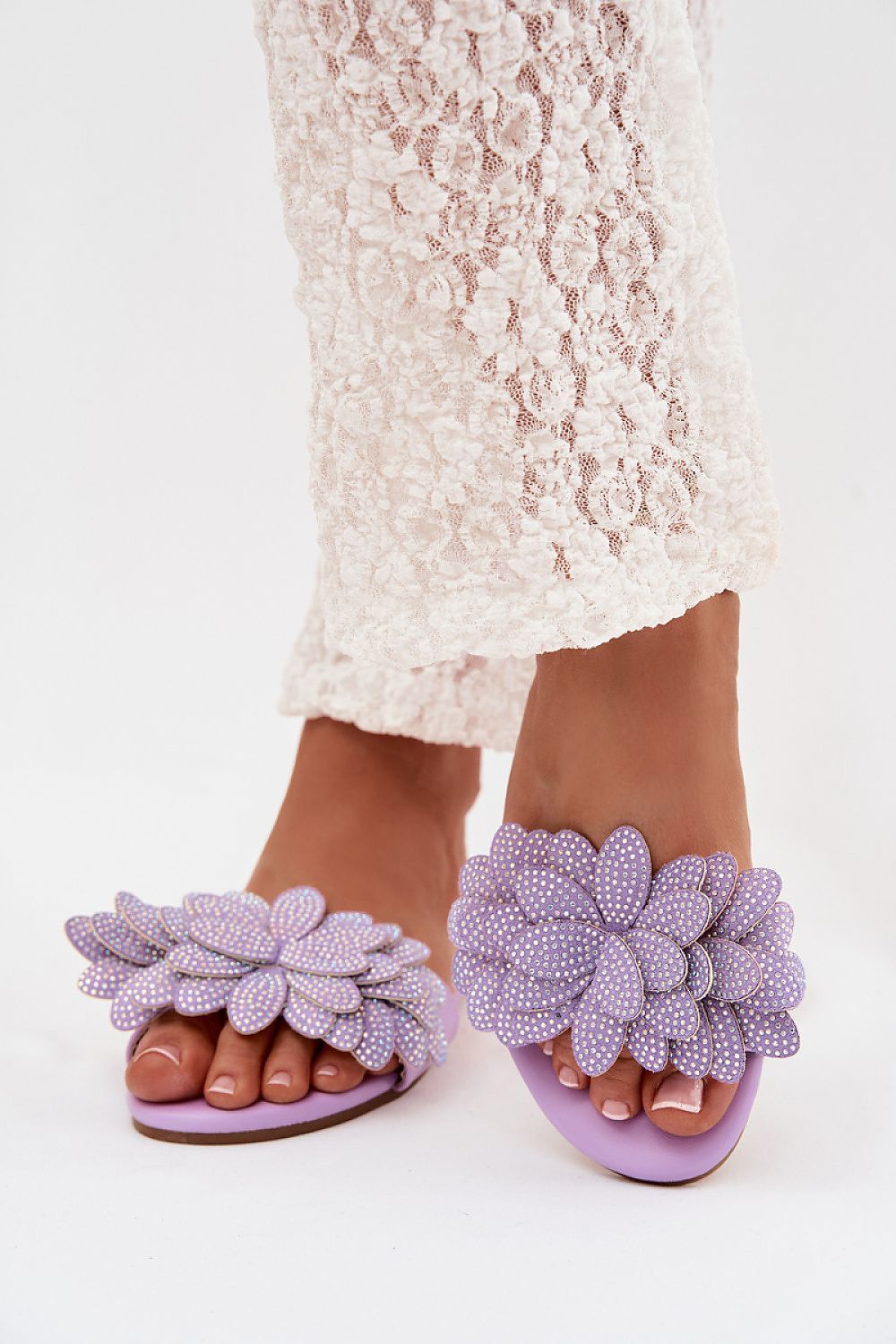 Purple floral sandals worn with a white lace dress on a white background