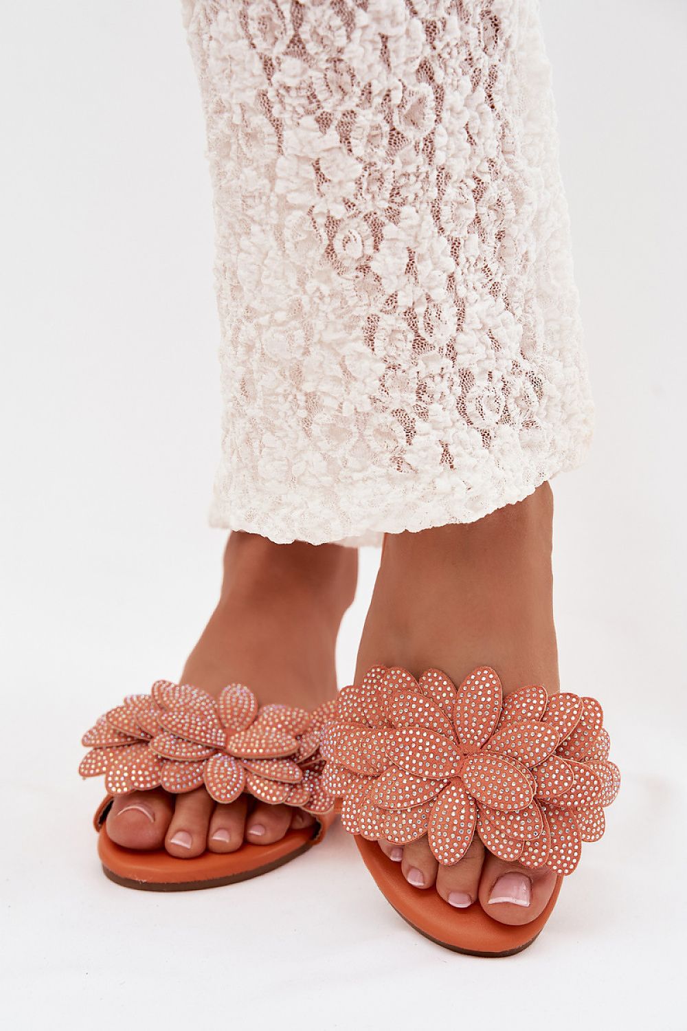 Peach sandals with floral designs worn with a white lace dress on a light background