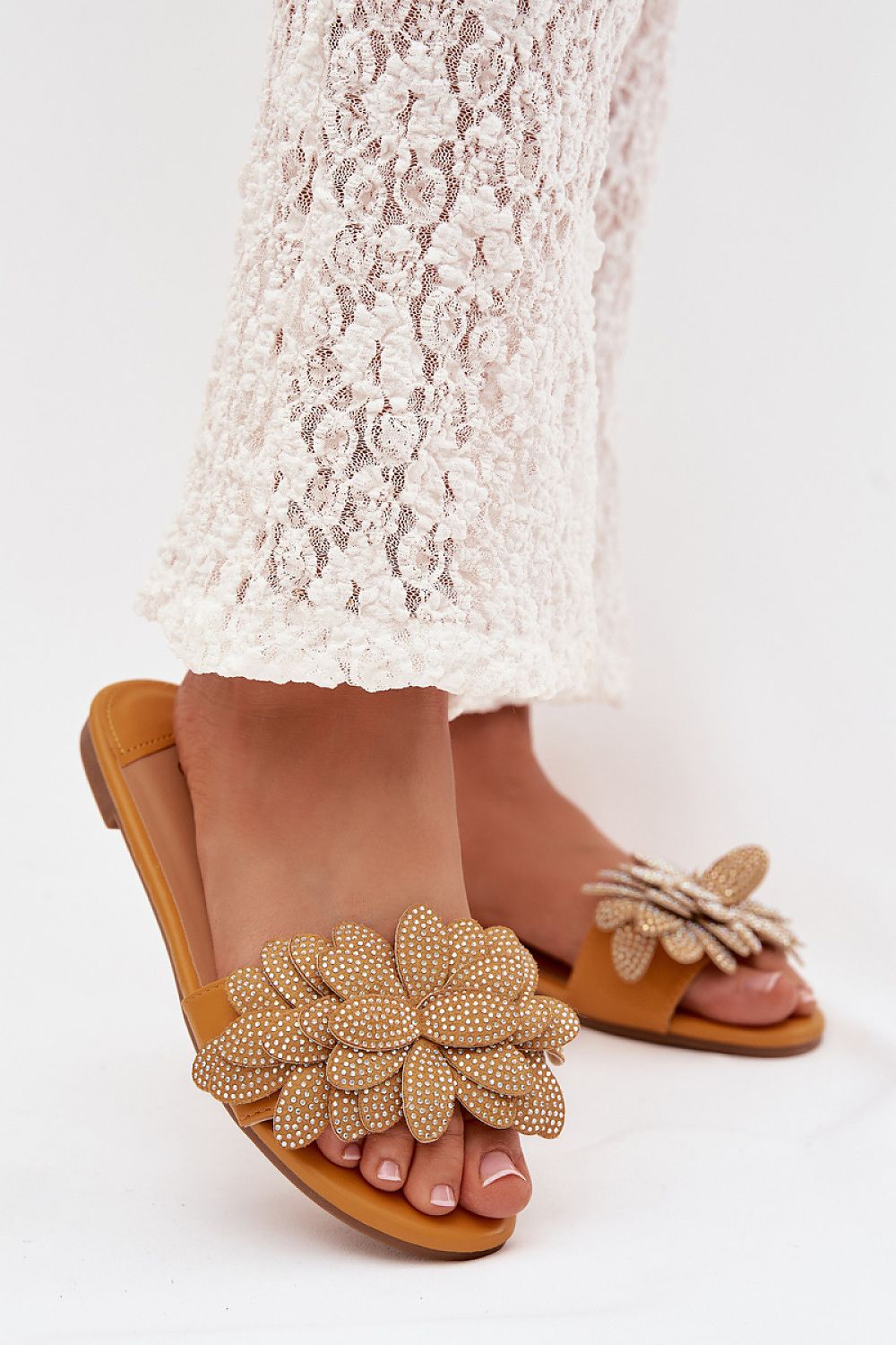 Brown sandals with floral embellishments worn with a white lace dress on a light background