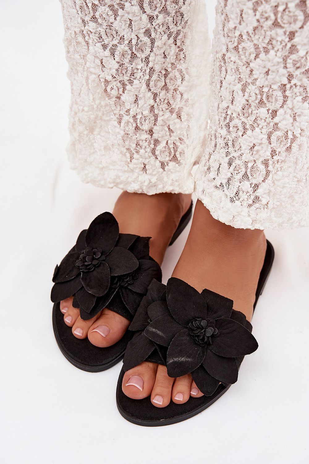 Black floral sandals worn with a white lace dress on a white background